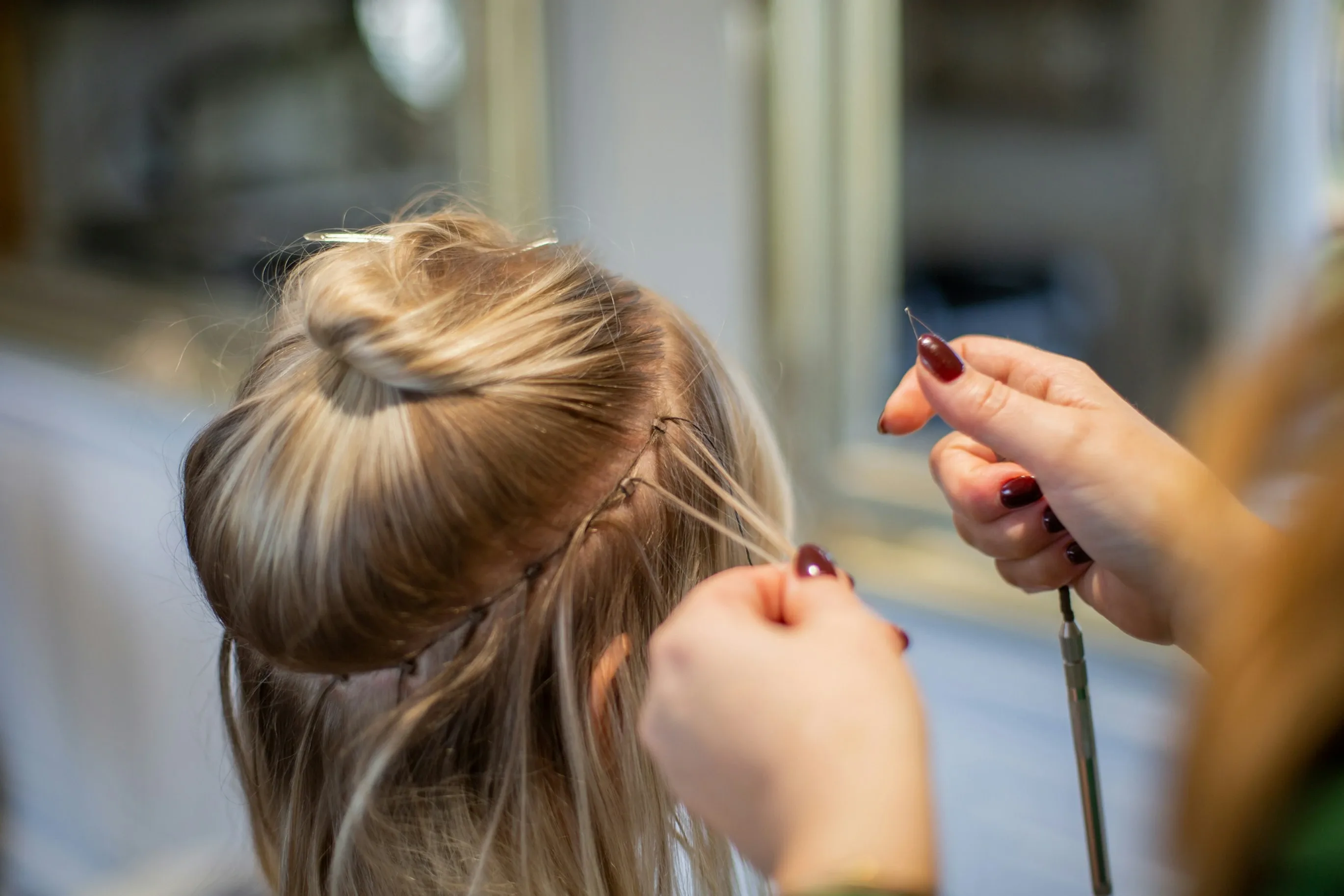 Technician sewing a hair extension weft onto a fine braid with a needle and thread